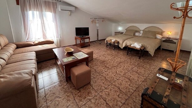 A hotel room with a sofa, a small table, a bed with a headboard, a television, and a floor lamp.