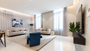 Een moderne woonkamer met een zithoek, een blauwe fauteuil, een salontafel en een wandgemonteerde flatscreen televisie.
