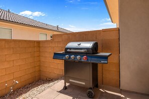 Een draagbare barbecue met een digitaal display en verschillende bedieningsknoppen, geplaatst op een terras met een bakstenen muur en een betegeld dak op de achtergrond.