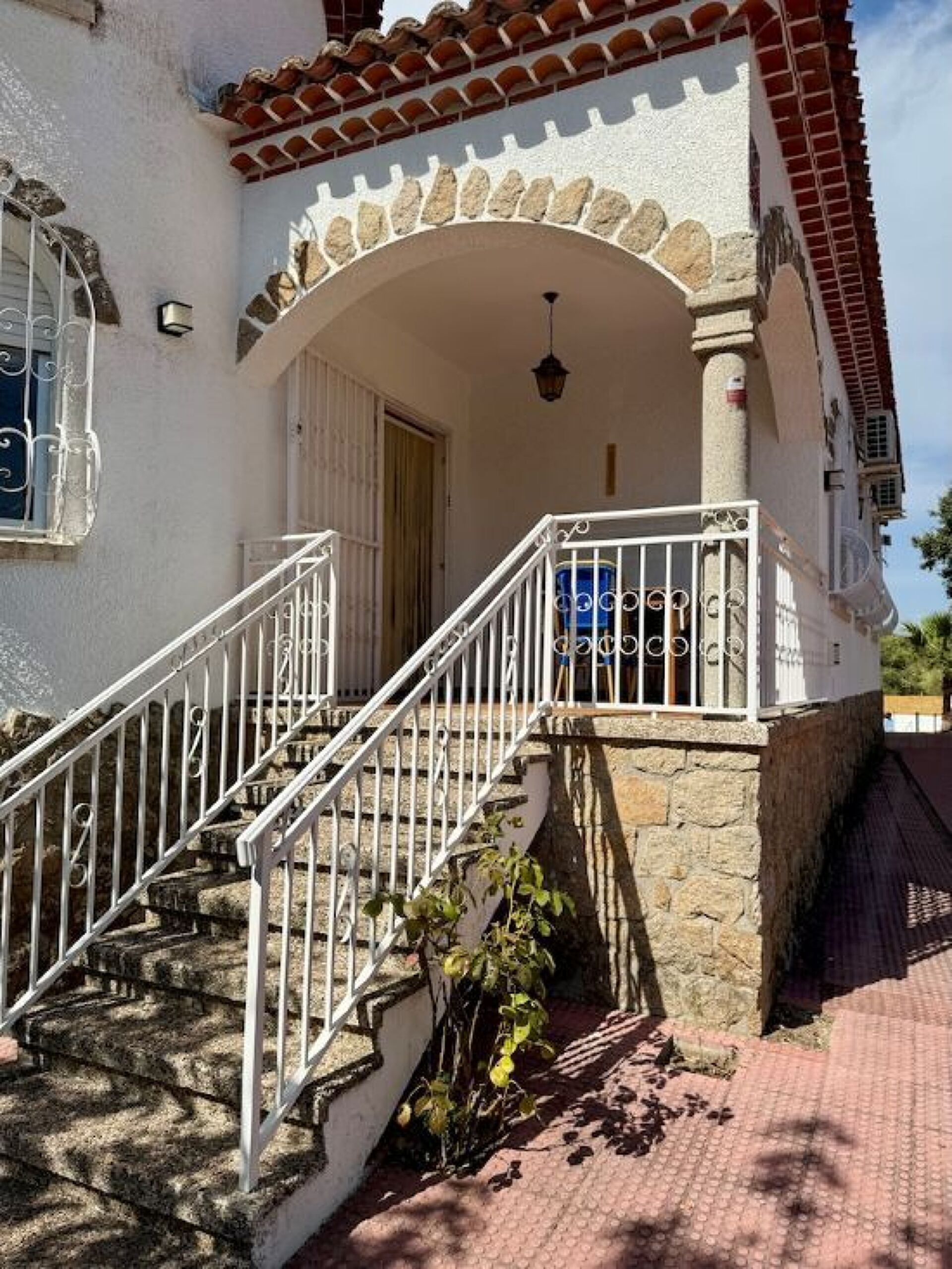 Un bâtiment dont la base est en pierre, les murs sont blancs, le toit est recouvert de tuiles et il possède un escalier blanc avec une rampe en métal.