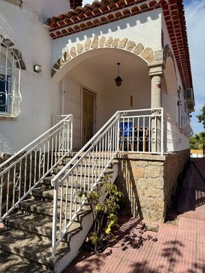 A building with a stone base, white walls, a tiled roof, and a white staircase with a metal railing.