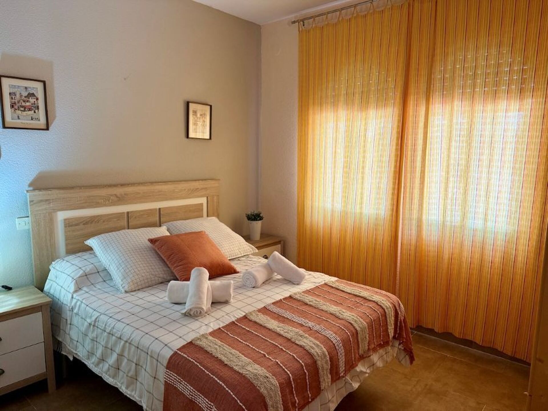 Une chambre d’hôtel avec un lit, une table de chevet, un tableau encadré au mur et une fenêtre avec des rideaux.