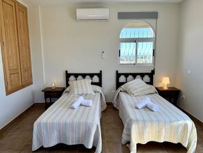 A hotel room with two single beds, a window with a view, an air conditioning unit, and a wooden wardrobe.