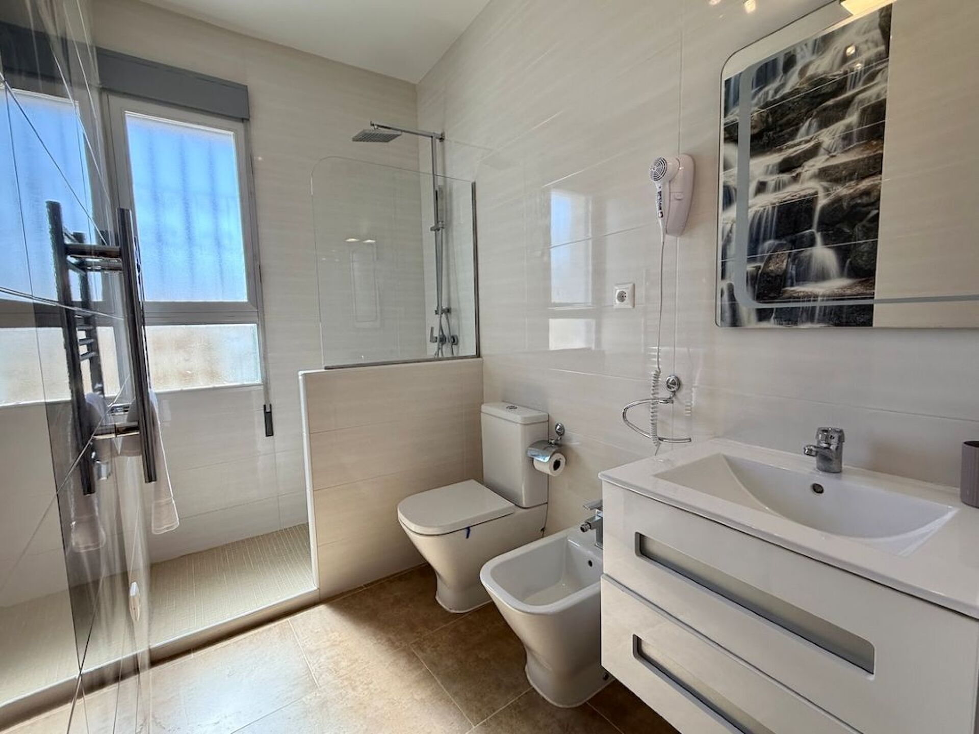 Une salle de bain moderne avec une douche à parois de verre, des toilettes, un bidet et un grand lavabo avec un miroir.