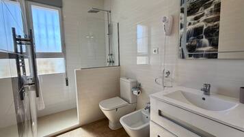 Une salle de bain moderne avec une douche à parois de verre, des toilettes, un bidet et un grand lavabo avec un miroir.