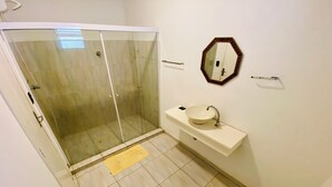 Un baño con ducha de vidrio, lavabo con espejo y un inodoro.