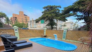 Una terraza de madera con piscina, sillas de descanso y una planta en maceta.