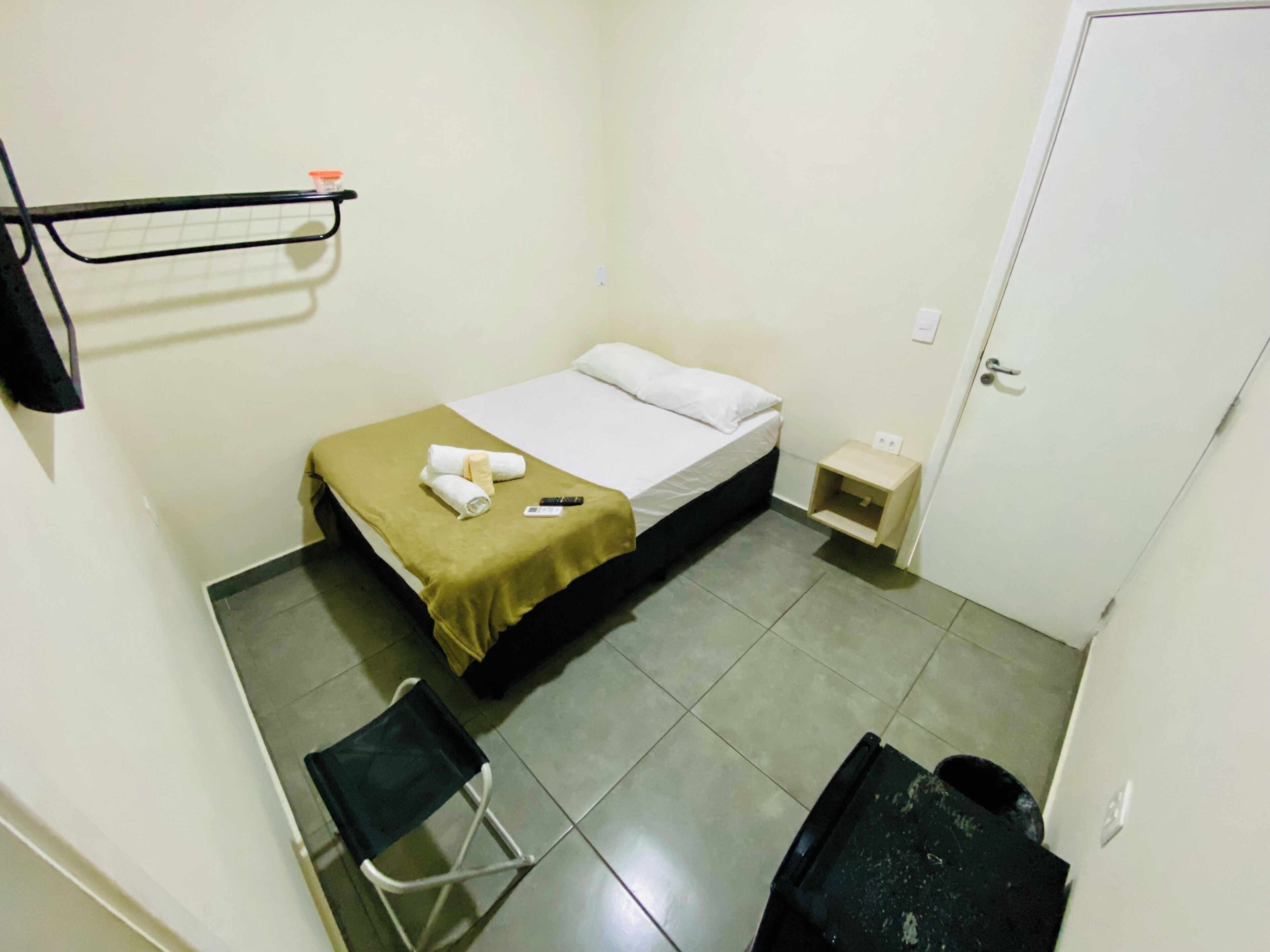 A small, clean room with a bed, a chair, a nightstand, and a door.