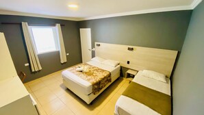 Habitación de hotel con una cama grande, una cama más pequeña, una mesita de noche, una ventana con cortinas y una puerta.