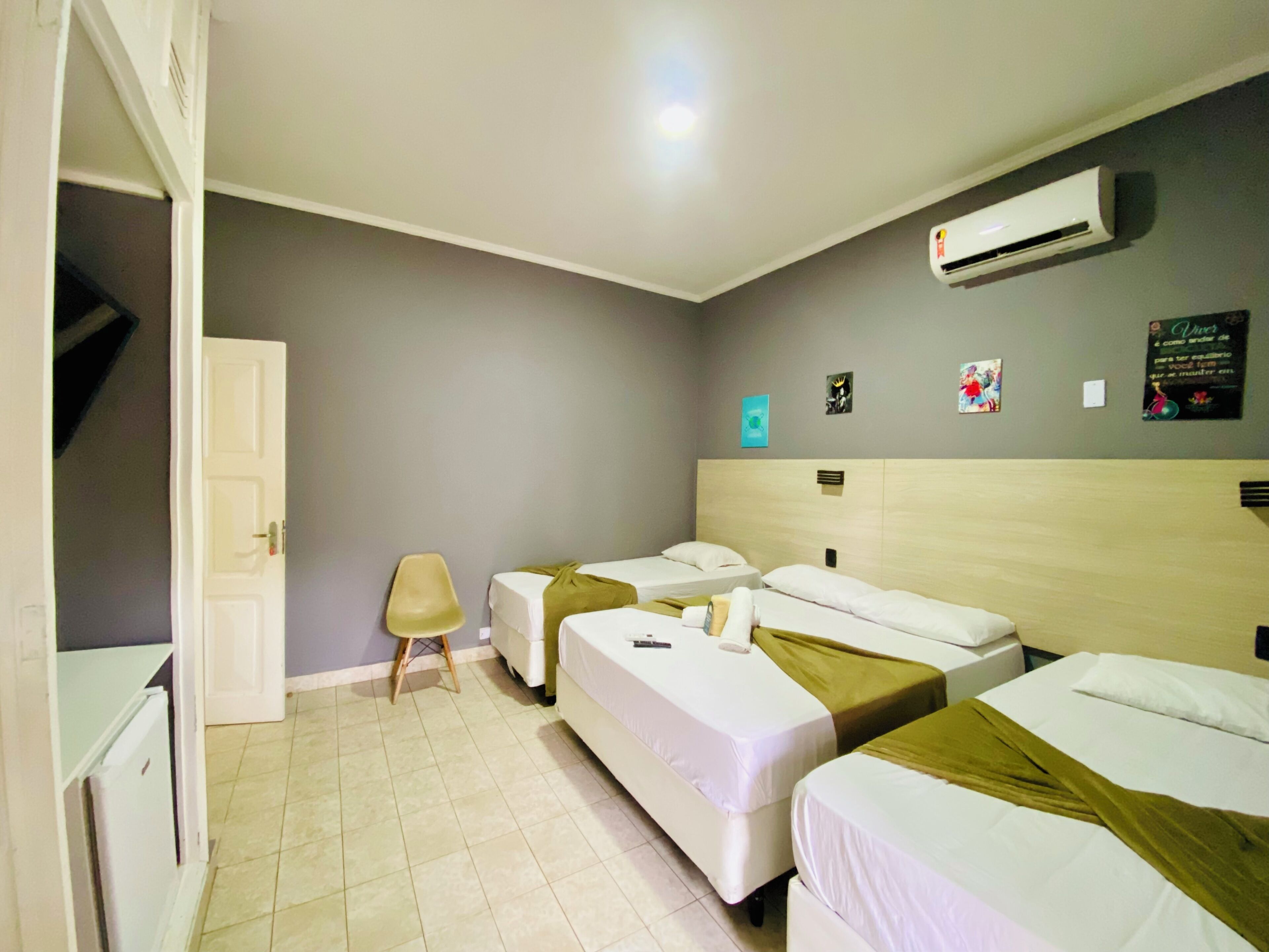 Hotelkamer met twee éénpersoonsbedden, een klein krukje, een airconditioning en een deur naar een andere kamer.