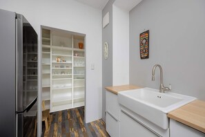 A compact kitchen with a built-in refrigerator, a white sink with a wooden countertop, and a storage cabinet with shelves. - Cosy Apartment with a Balcony | 2 Bedrooms | Workspace (Warszawa)