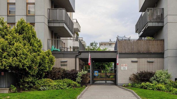En modern byggnad med en grind vid entrén, flera balkonger och ett välskött trädgårdsområde.