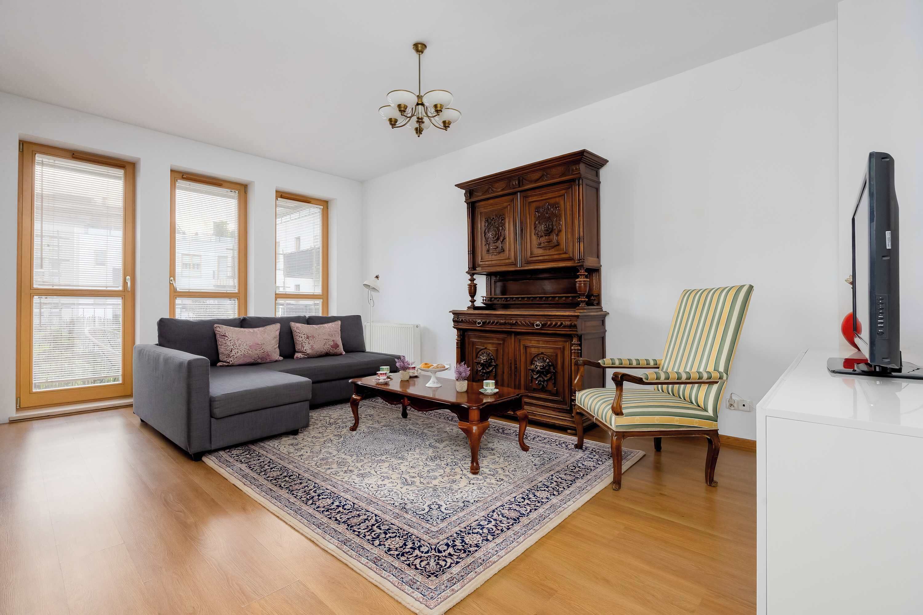 Una sala de estar con un sofá, una mesa de centro, un tapete estampado, un aparador de madera y un sillón a rayas.