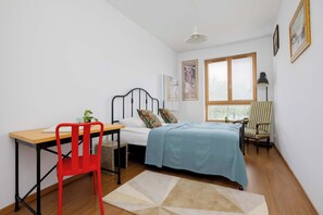 A bedroom with a bed, a desk, a chair, a window with blinds, and a lamp. - Cosy Apartment with a Balcony | 2 Bedrooms | Workspace (Warszawa)
