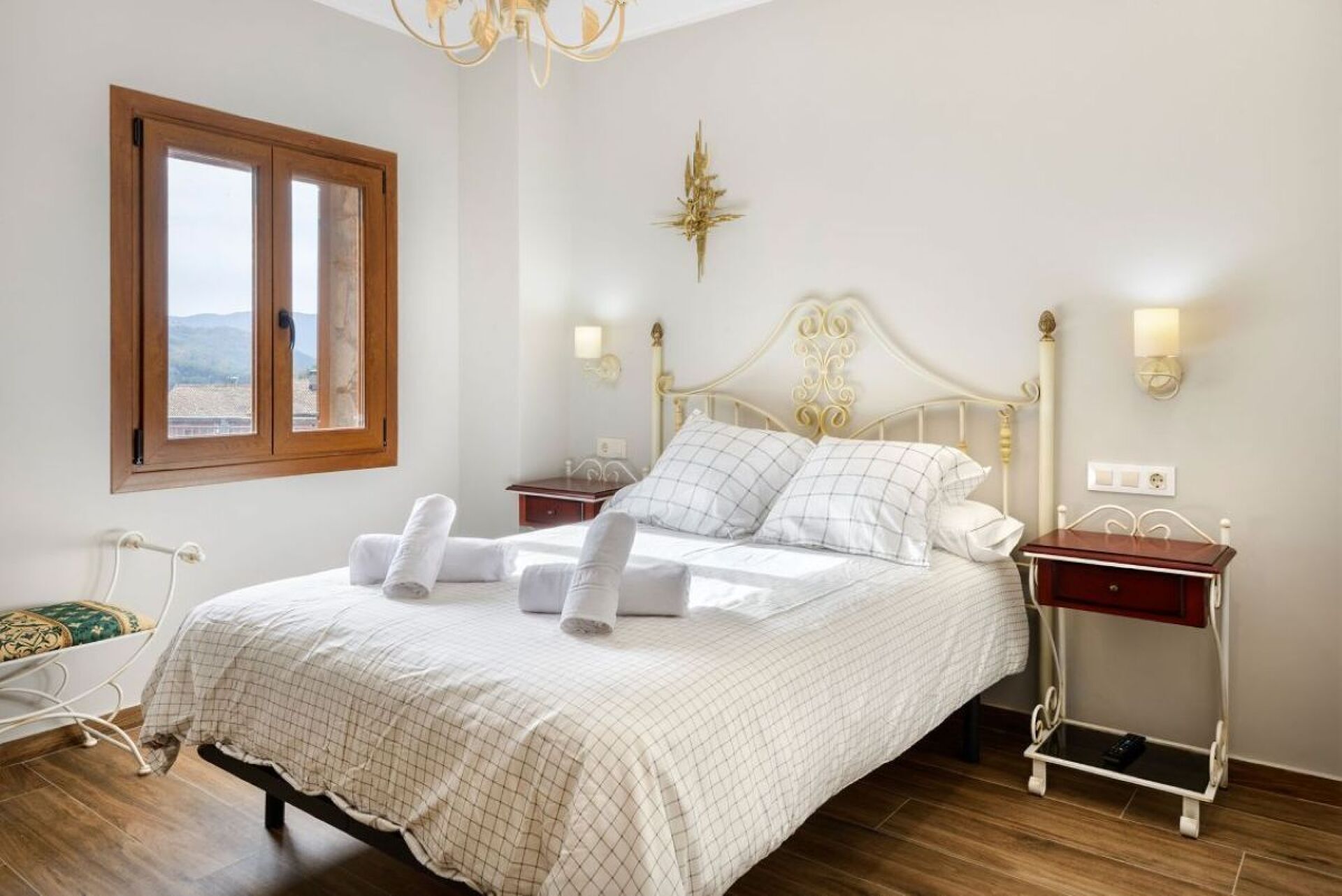 Un lit bien fait, avec du linge de lit et des serviettes blanches, une tête de lit en bois, des tables de chevet avec des lampes et une fenêtre donnant sur un beau paysage.