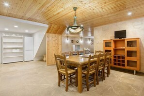 A dining area with a wooden table and chairs, a chandelier, and a television on a cabinet.