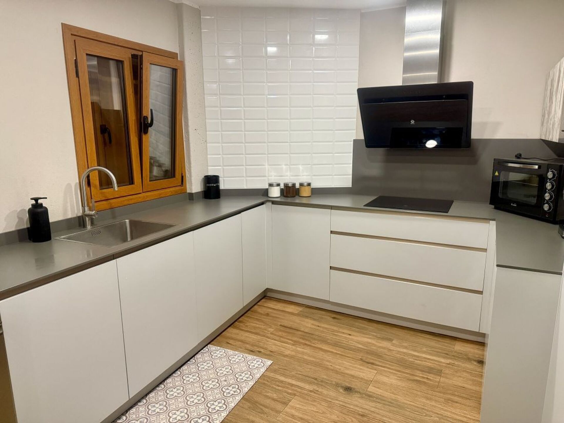 Een moderne keuken met witte kasten, een roestvrijstalen spoelbak, een zwarte afzuigkap en een inbouwmagnetron.