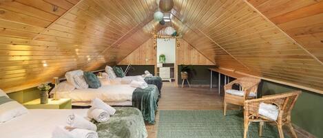 A cozy attic bedroom with a sloped ceiling, two beds, a chair, and a small table.