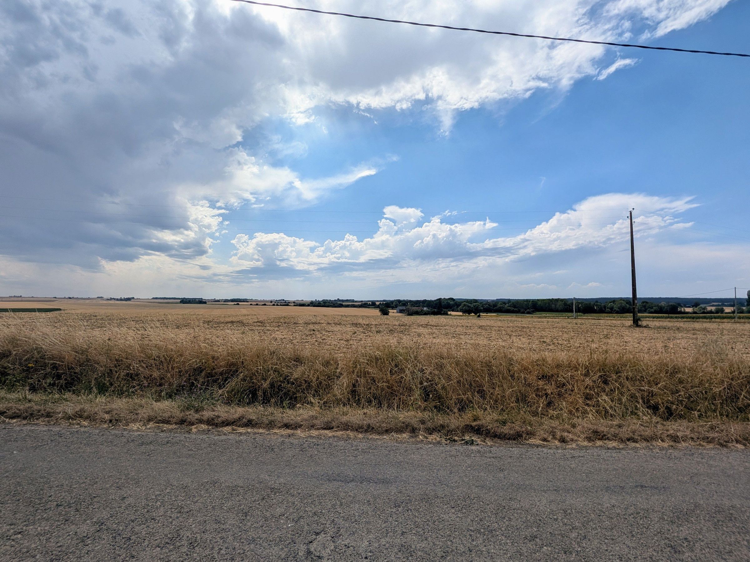 Un paysage rural avec un ciel dégagé, une ligne électrique et une route au premier plan.
