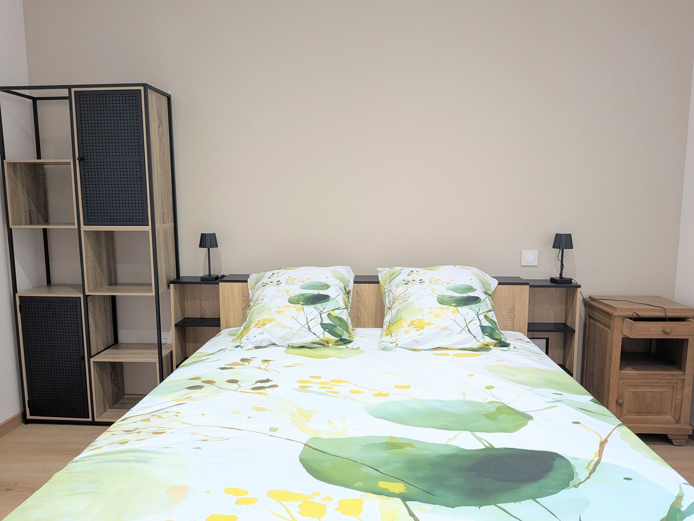 Une chambre à coucher comprenant un lit, deux tables de chevet, une armoire en bois et une étagère fixée au mur.