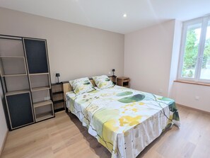 A bedroom with a bed, a wardrobe, a nightstand, a window, and a door.