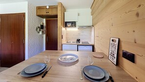 A dining table set with plates, cutlery, and glasses, with a kitchen in the background. - Studio at ski slopes, Mont Blanc view (Combloux)