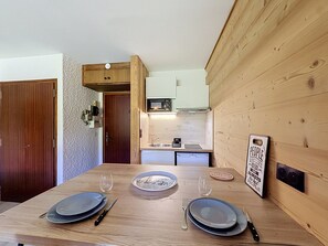 A dining table set with plates, cutlery, and glasses, with a kitchen in the background. - Studio at ski slopes, Mont Blanc view (Combloux)