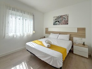 A hotel room with a bed, a bedside table with a lamp, a wall-mounted artwork, and a window with sheer curtains. - Apartment in Salou near the beach - 5 guests (Salou)