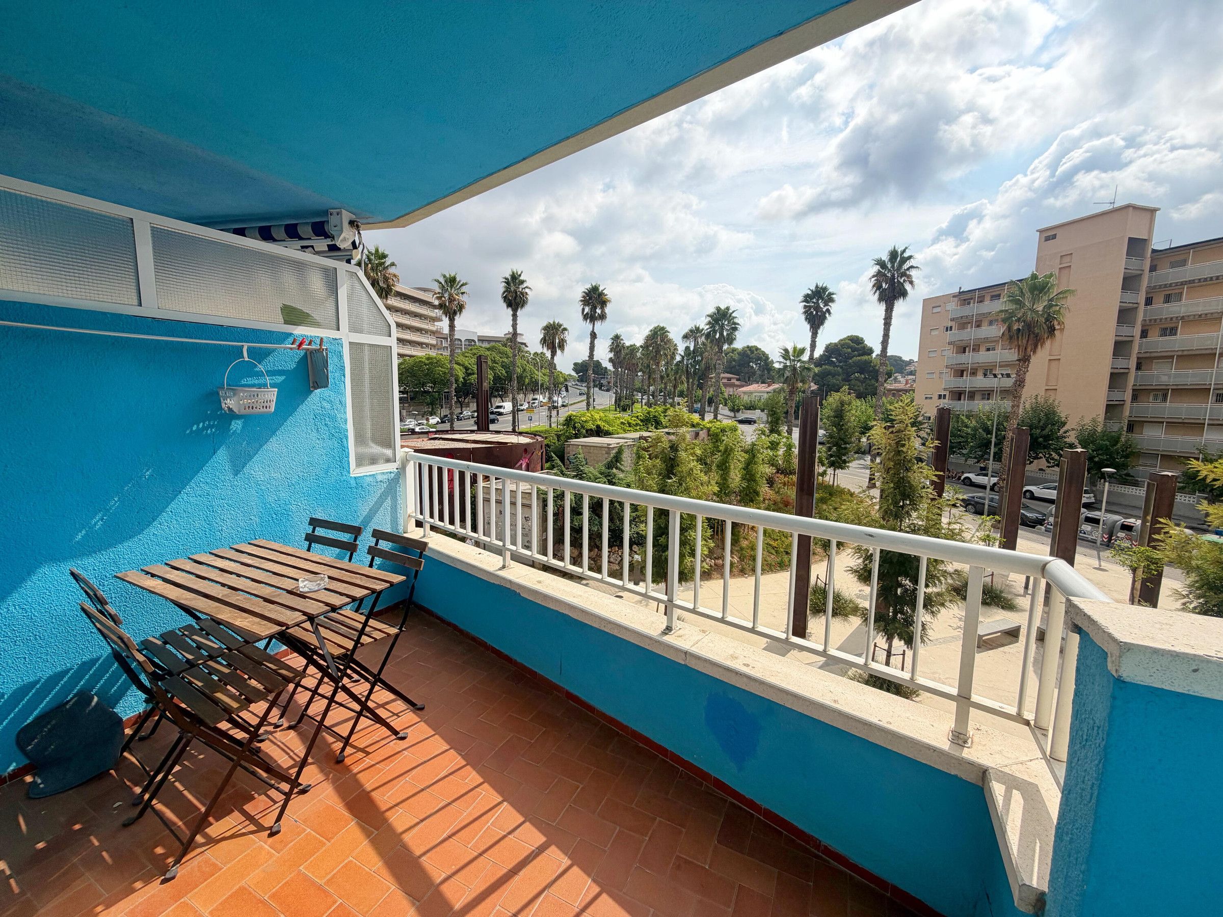 Un balcon avec une piscine, un espace salon extérieur et une vue sur les palmiers et les bâtiments.