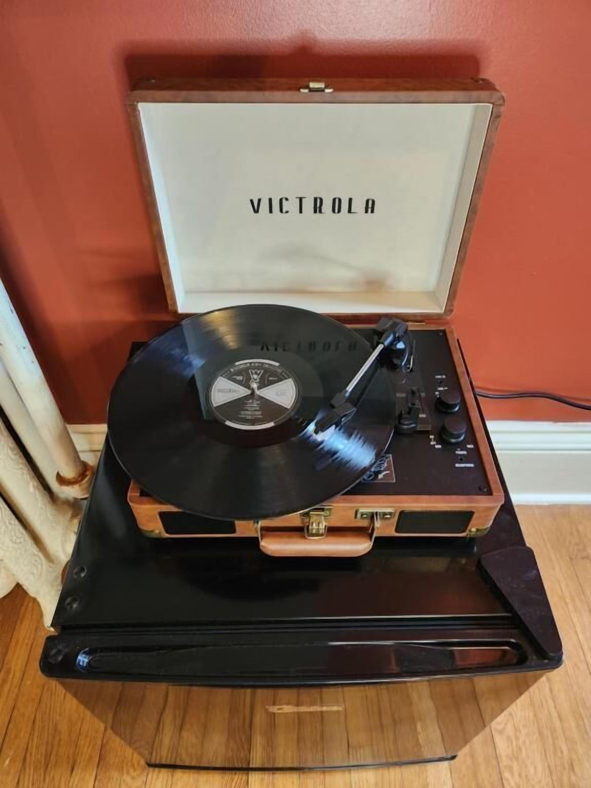A turntable with a vinyl record on a wooden cabinet against a red wall.