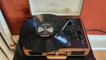 A turntable with a vinyl record on a wooden cabinet against a red wall.