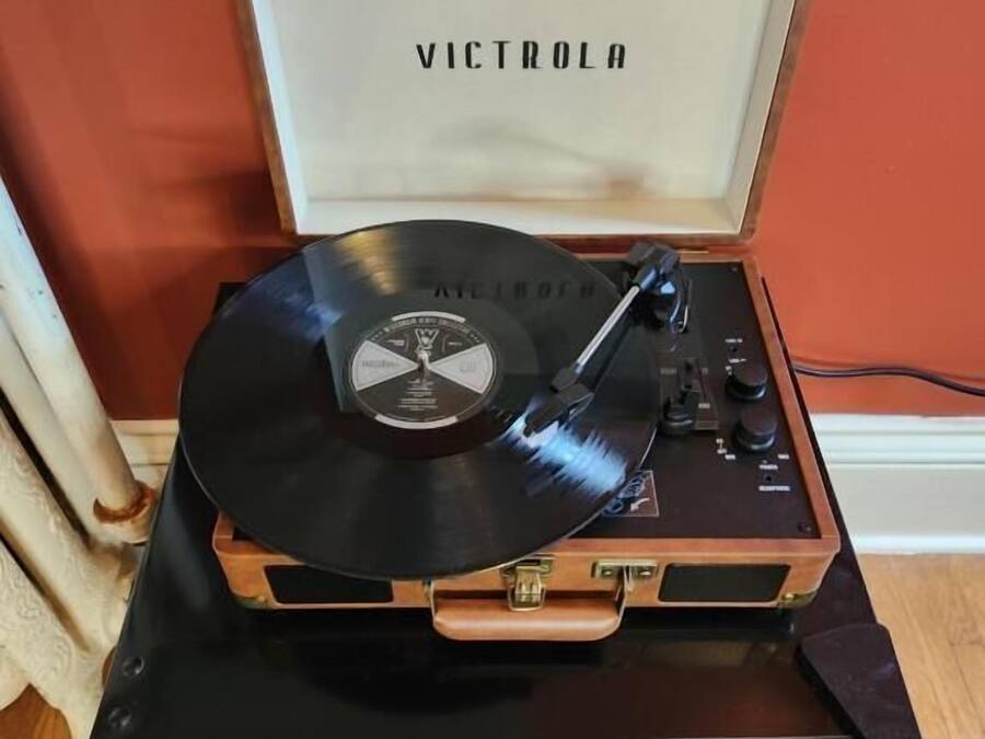 A turntable with a vinyl record on a wooden cabinet against a red wall.