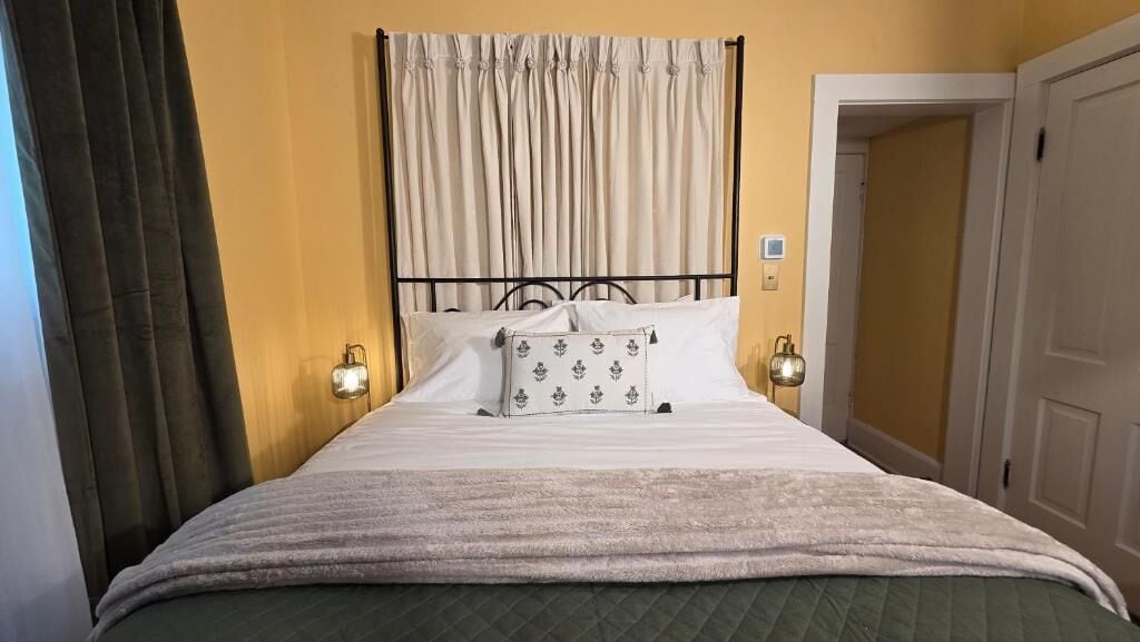 Una cama con cabecera, dos lámparas de noche y una ventana con cortinas.