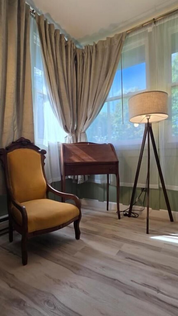 A room with a wooden floor, a yellow armchair, a small wooden table, a floor lamp, and a window with curtains.