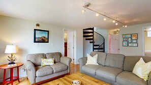 A living room with two sofas, a small table with a lamp, a staircase, and a door leading to another room. - Waterfront Retreat with Private Dock, Kayaks & Stunning Water Views (Phippsburg)