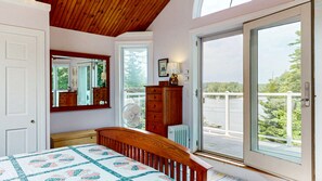 A bedroom with a bed, a dresser, a mirror, a window, and a view of a body of water. - Waterfront Retreat with Private Dock, Kayaks & Stunning Water Views (Phippsburg)