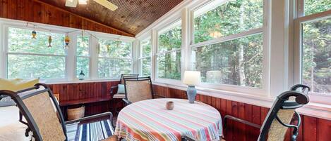 A wooden-paneled room with a round table, chairs, and large windows.