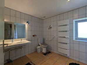 Een badkamer met witte betegelde wanden, een wit wastafelmeubel, een toilet, een douchegedeelte en een raam.