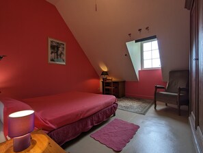 A bedroom with a sloped ceiling, a bed with a red bedspread, a chair, a small table with a lamp, and a window with a view of the outside. - Country house in Lourouer-Saint-Laurent (Lourouer-Saint-Laurent)