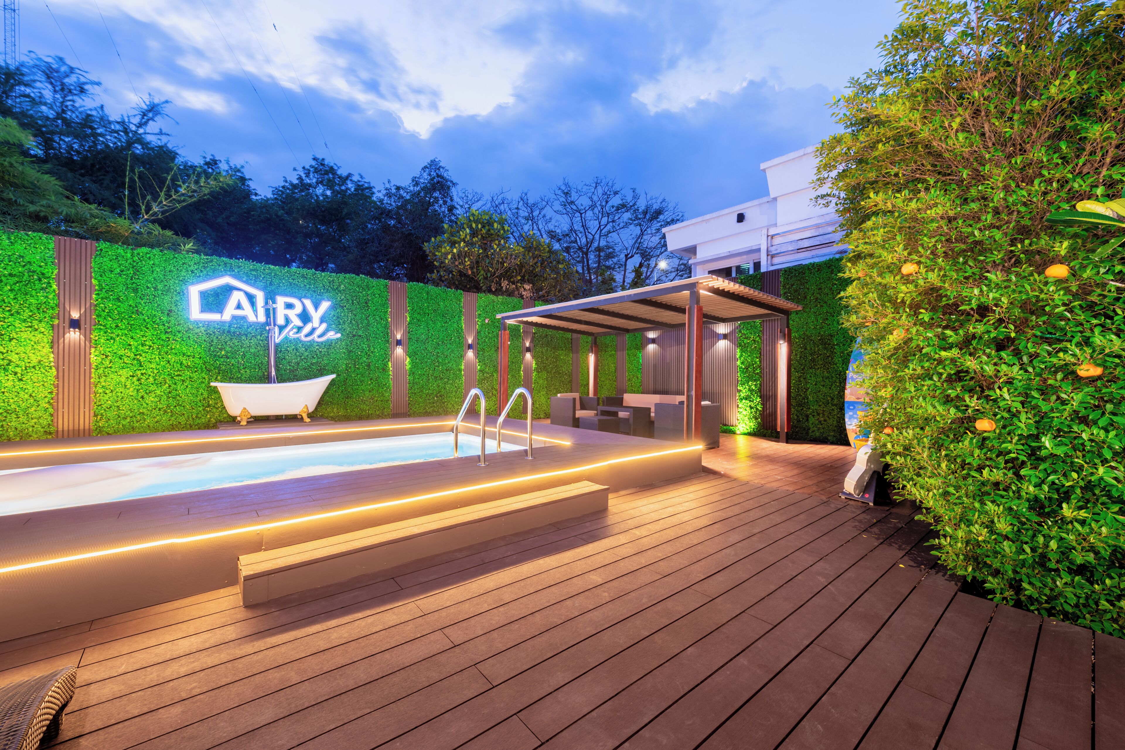 A modern outdoor pool area with a neon sign, wooden deck, and a covered seating area.