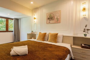 A hotel room with a large bed, a bedside table, a nightstand, a window with curtains, and wall-mounted lighting.