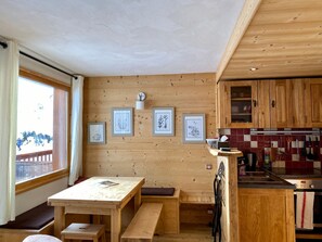 A wooden interior with a dining area, kitchen, and a window with a view. - Cozy duplex, 6 guests, slope view (Plagne Villages)