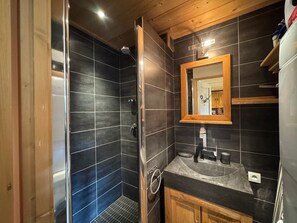 Un baño con baldosas oscuras, un tocador de madera, un lavamanos y un espejo.