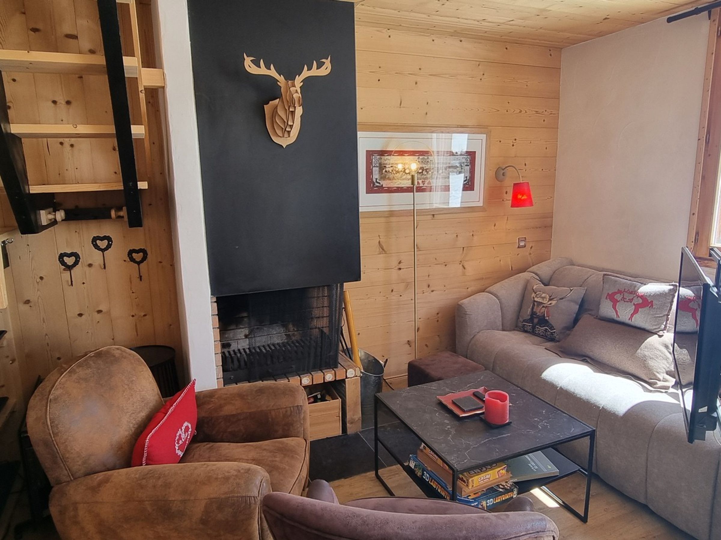 A cozy living room with a fireplace, wooden walls, a sofa, and a coffee table with books and a mug.