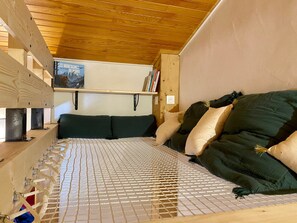 Een houten stapelbed met metalen frame, een matras met wit raster en een wandplank met boeken en een ingelijste foto.