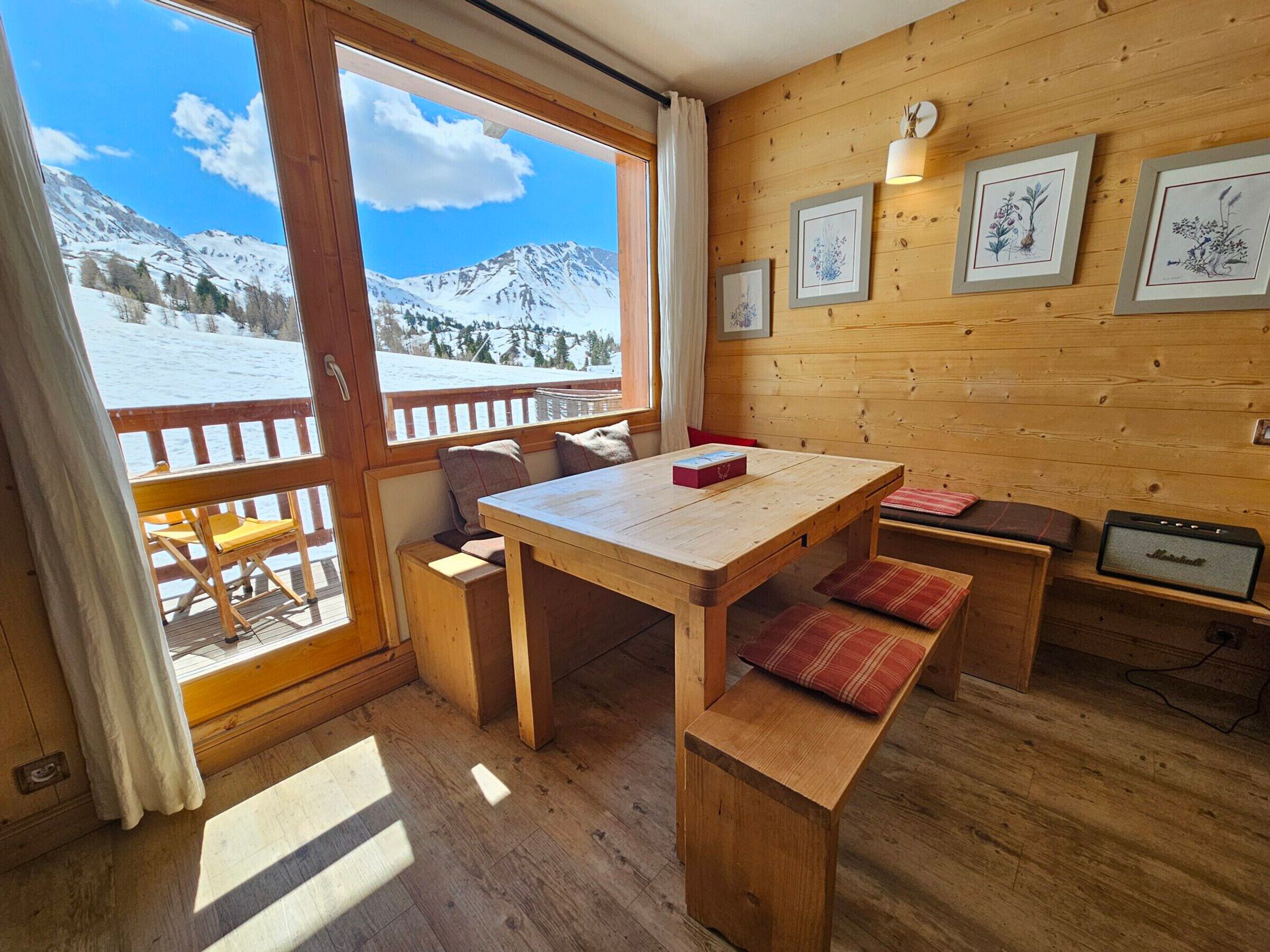 Interior de madeira com uma mesa, bancos e impressões botânicas emolduradas na parede.