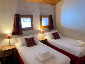 Una habitación de hotel con dos camas individuales, cada una con colcha y almohadas rojas a juego. Hay dos mesitas de noche con lámparas, y el techo es de madera.