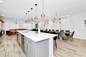 A modern kitchen with a central island, pendant lighting, and a dining area with a long table. - UFC Champion José Aldo’s 9-BR Near to Disney (Kissimmee)