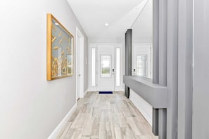 Ein moderner Flur mit hellem Boden, einem gerahmten Kunstwerk links und einer Tür mit Fenster rechts.