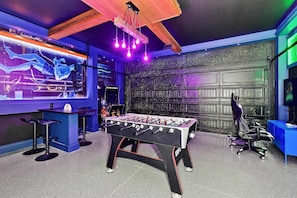 Ein Zimmer mit einem Kicker, einem Gaming-Sessel und einem Fernseher, der ein Spiel zeigt.